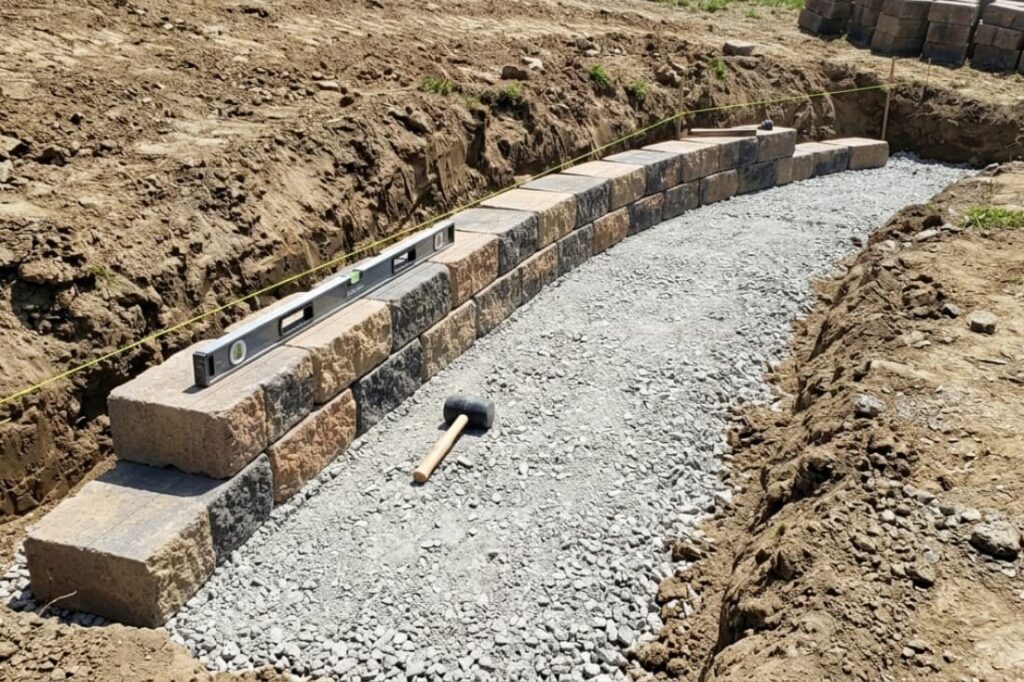 Under-construction curved retaining wall designs with segmental blocks, gravel base, level tool, and rubber mallet.